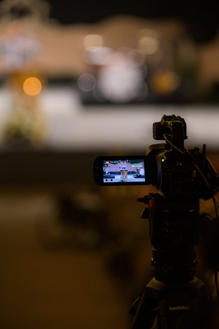 Close-up of a camera on a tripod recording a performance in a dimly lit studio setting.
